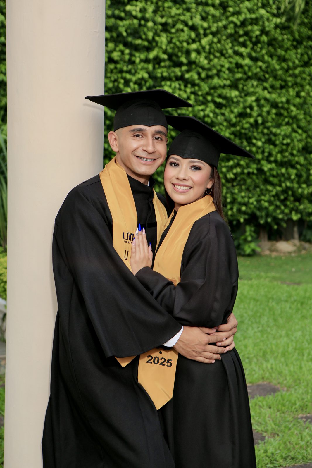 Pareja de graduados con toga y birrete en jardín